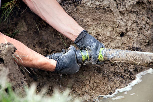 Person in gloves fixing a pipe in dirt.