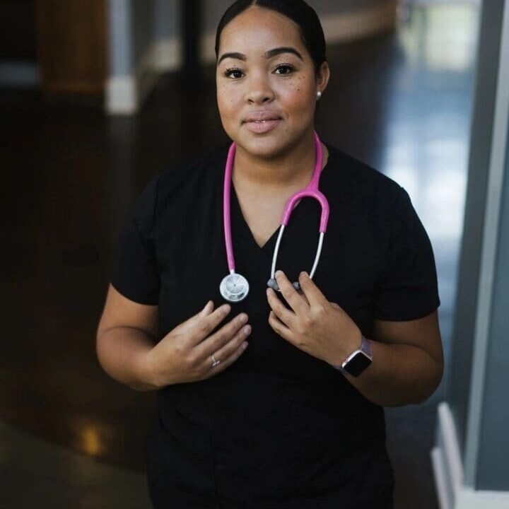 Woman in black scrubs with pink stethoscope.